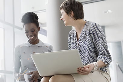 Black Caucasian professional women sitting talking smiling.